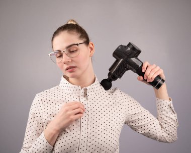 Beyaz bir kadın sırt ve omuzlarında ağrı için masaj tabancası kullanıyor.