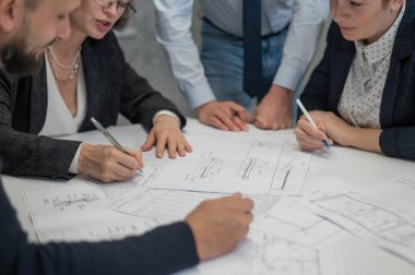 Ofisteki masanın üzerinde planları olan dört meslektaşın ellerinin yakın çekimi. Mühendis ve mimarların beyin fırtınası