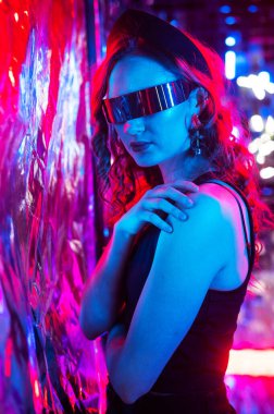 Güneş gözlüklü beyaz kadın neon stüdyoda poz veriyor.