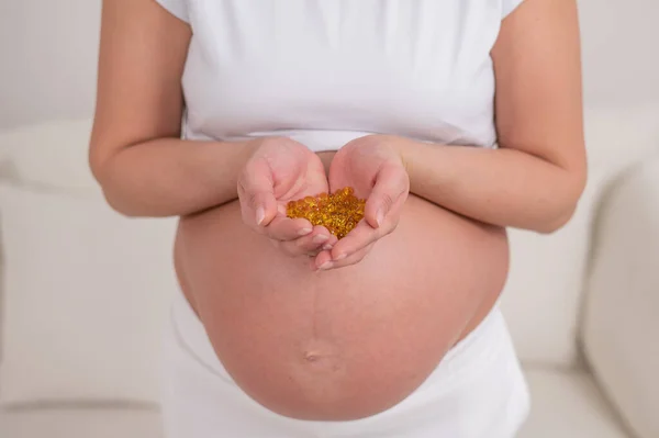 裸の腹を持つ妊婦はビタミンの一握りを保持します 透明な黄金の丸薬 期待する母親のためのビタミンD — ストック写真