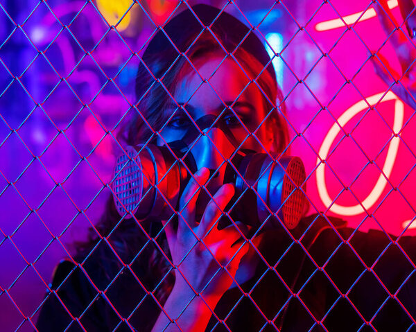 Caucasian woman in a gas mask behind a fence in a neon studio