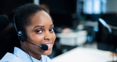Afrikalı genç bir kadın kulaklıkla bir müşteriyle konuşuyor. Çağrı merkezinin kadın çalışanı