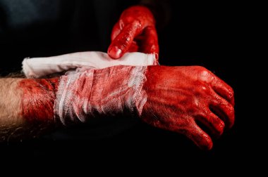 Kanla kaplı bir adam ellerini bandajlıyor.