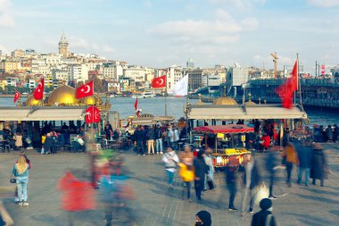 EMINONU, ISTANBUL / TURKEY - NOVEMBER 15, 2021: People walk across the square and relax in a small cafe on Eminonu pier. Long exposure, blurred motion
