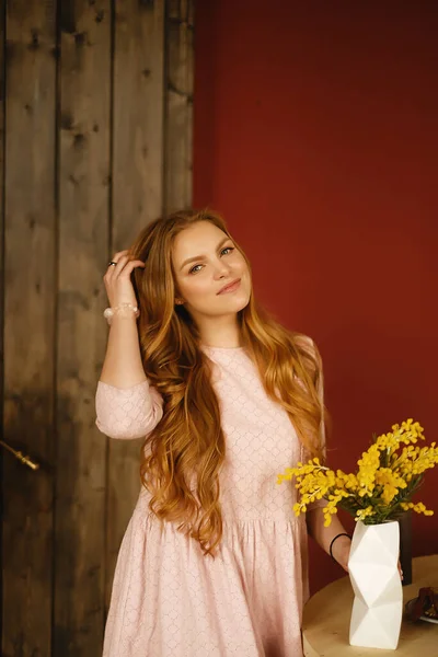 Молодая кавказская женщина с длинными светлыми волосами, в длинном розовом платье в стильной квартире, девушка с цветами — стоковое фото