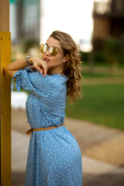 Portrait d'une jeune femme caucasienne aux cheveux bouclés dans une longue robe bleue, dame européenne à lunettes dans une rue d'été — Photo