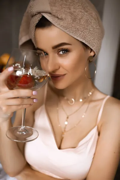 Молодая белая женщина ест фрукты на завтрак, красивая леди с полотенцем на голове, девушка со стаканом воды, утренний ритуал — стоковое фото