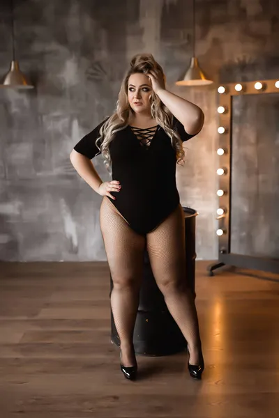 Femme de grande taille avec de longs cheveux blonds en lingerie, blonde en surpoids avec des formes luxuriantes dans le grenier, fille pleine en vêtements noirs avec un maquillage lumineux — Photo