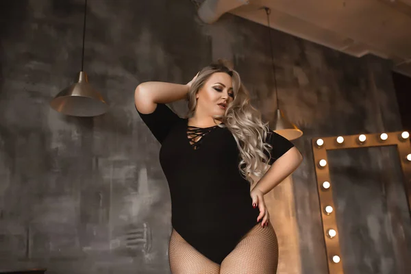 Plus-size woman with long blond hair in lingerie , overweight blonde with lush forms in the loft, full girl in black clothes with bright makeup — Stock Photo, Image