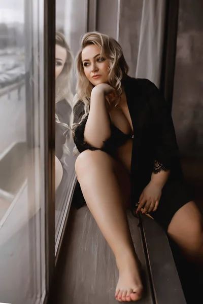 Plus-Size-Frau mit langen blonden Haaren in Dessous, übergewichtige Blondine mit üppigen Formen auf dem Dachboden, volles Mädchen in schwarzer Kleidung mit hellem Make-up — Stockfoto