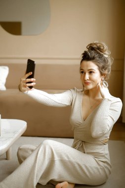 Şık bir dairede oturan beyaz bir kadın telefonuna bakıyor. Yerde oturmuş e-posta yazan şık bir bayan. Minimalist bir dairede elinde telefon olan bir kız blog yazarı.