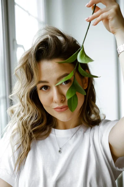 Portrait d'une jeune femme caucasienne avec une branche verte, belle fille bien entretenue avec une fleur, photo esthétique d'une dame en vêtements blancs avec une feuille verte — Photo
