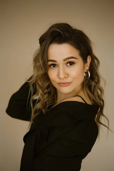 Retrato de mujer caucásica joven belleza en un traje negro, una chica con maquillaje y pelo rizado en chaqueta, una señora de ojos oscuros con pendientes-anillos y maquillaje brillante sobre fondo claro — Foto de Stock