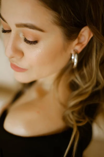 Retrato de jovem mulher caucasiana beleza em um terno preto, uma menina com maquiagem e cabelos encaracolados na jaqueta, uma senhora olhos escuros com brincos-anéis e maquiagem brilhante no fundo claro — Fotografia de Stock