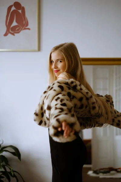 Portrait of a young caucasian woman with long blond hair wearing a leopard fur coat, beautiful slim girl in a dress and fur coat in a stylish apartment, bright lady with makeup in a New Years — Stock Photo, Image