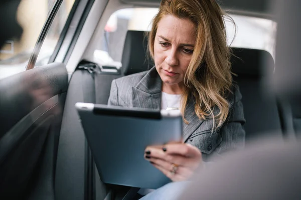 若いビジネスマンの女性は 車の後部座席に座って 慎重に彼女の仕事のスケジュールを整理するためにタブレットを使用しています — ストック写真