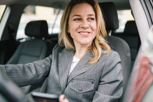 若いビジネス女性は会社の車を運転し 彼女の電話をチェックし 窓の外を見る — ストック写真