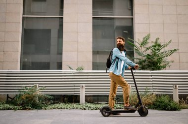 Young hipster man driving electric scooter after work. Ecological transportation concept.