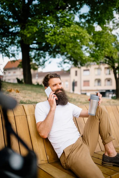 Photo of a man sitting on the bench talking on your mobile and drinking coffee