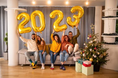 Gündelik giysiler içinde altın renkli sayılar taşıyan ve gülümseyen bir grup genç insan.