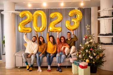 Gündelik giysiler içinde altın renkli sayılar taşıyan ve gülümseyen bir grup genç insan.