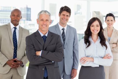 Smiling business team standing in front of a bright window clipart