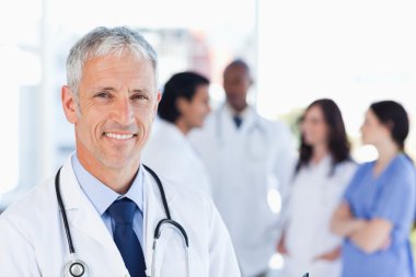 Mature doctor standing upright while waiting for his team clipart