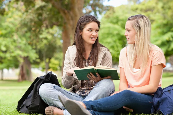 Adolescentes do sexo feminino sentadas enquanto estudavam com um livro didático — Fotografia de Stock
