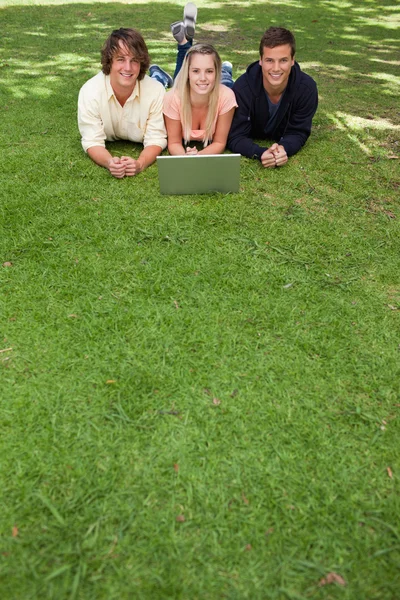 Three smiling students lying in a park — Stock Photo, Image