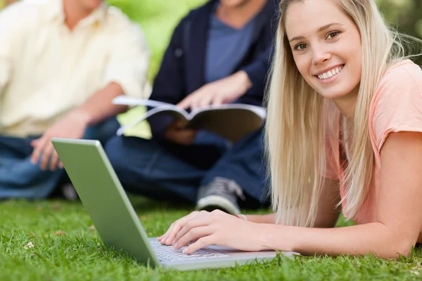 Portrait of a smiling girl using a laptop while lying in a park — Stock Photo, Image