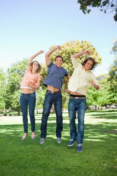 Three students jumping while raising an arm — Stockfoto