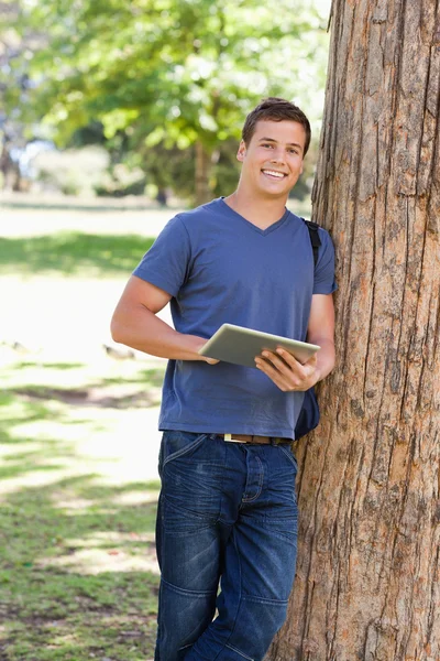 Bir dokunuş kullanırken karşı bir ağaca yaslanmış bir öğrenci portresi — Stok fotoğraf