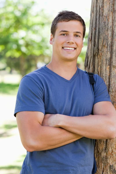 Крупный план улыбающегося молодого человека, прислонившегося к дереву — стоковое фото