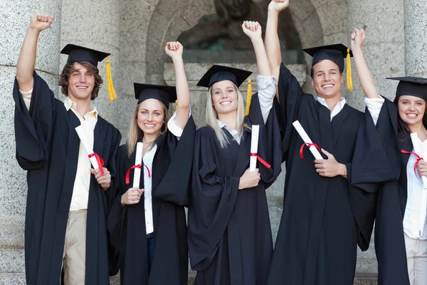 Graduados sorridentes posando enquanto levantam os braços — Fotografia de Stock