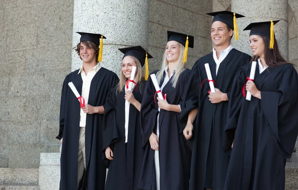Graduados sonrientes posando mientras sostienen su diploma — Foto de Stock