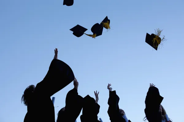 Cinco graduados lanzando sus sombreros al cielo — Foto de Stock