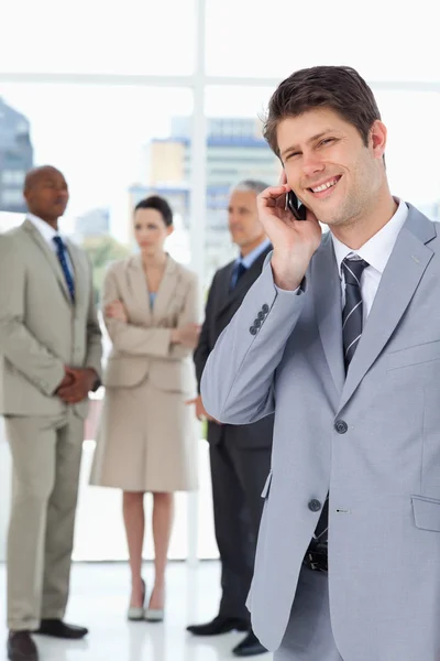 Un hombre de negocios sonriente usando un teléfono móvil frente a su equipo —  Fotos de Stock
