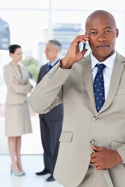 Jonge manager praten over de telefoon zeer serieus terwijl zijn team — Stockfoto