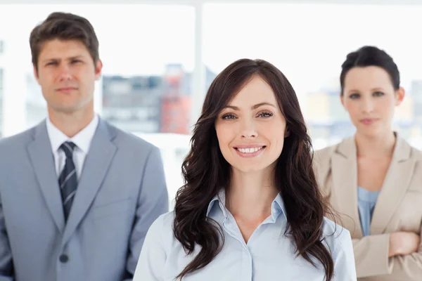 Young smiling woman standing in front of two co-workers — Stock Photo, Image