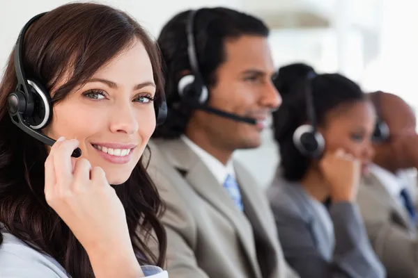 Lächelnder Mitarbeiter, der mit einem Headset arbeitet, während er auf die Kamera blickt — Stockfoto