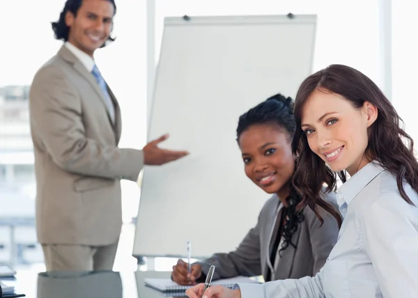 Two young smiling employees sitting at the desk with a colleague — Stock Photo, Image