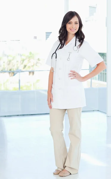 Unga leende sjuksköterska stående upprätt med ena handen på hennes höft — Stockfoto