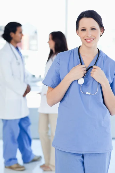 Giovane sorridente medico stagista indossa la sua uniforme e in piedi in — Foto Stock