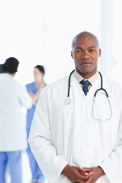 Doctor standing upright with his hands crossed and his team in t — Stock Photo, Image