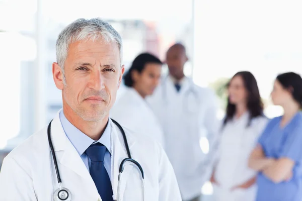 Maturo medico guardando dritto davanti mentre la sua squadra è alla ricerca di un — Foto Stock