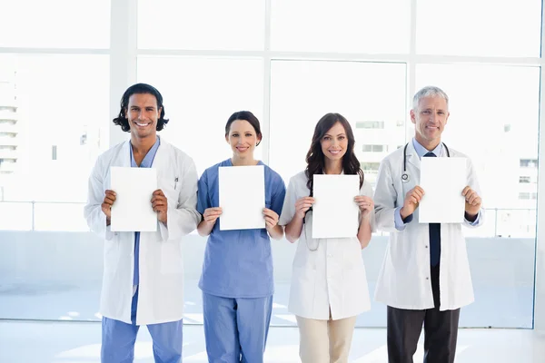 Four medical standing upright while holding blank sheets — Stock Photo, Image