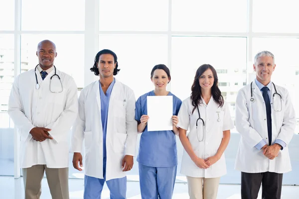 Équipe médicale debout autour d'un stagiaire qui tient un blanc — Photo