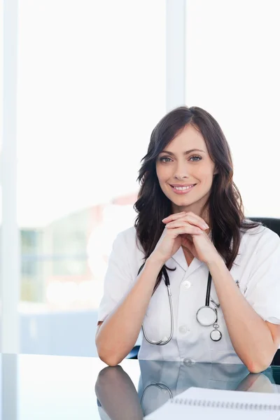 Médico sonriente sentado en el escritorio con los codos sobre la mesa —  Fotos de Stock