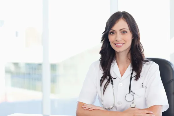 Jonge dokter zittend op een zwarte stoel aan de balie met haar armen — Stockfoto