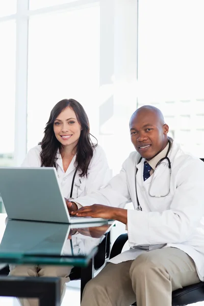 Sorrindo médico trabalhando em um laptop, enquanto acompanhado por seu coll — Fotografia de Stock